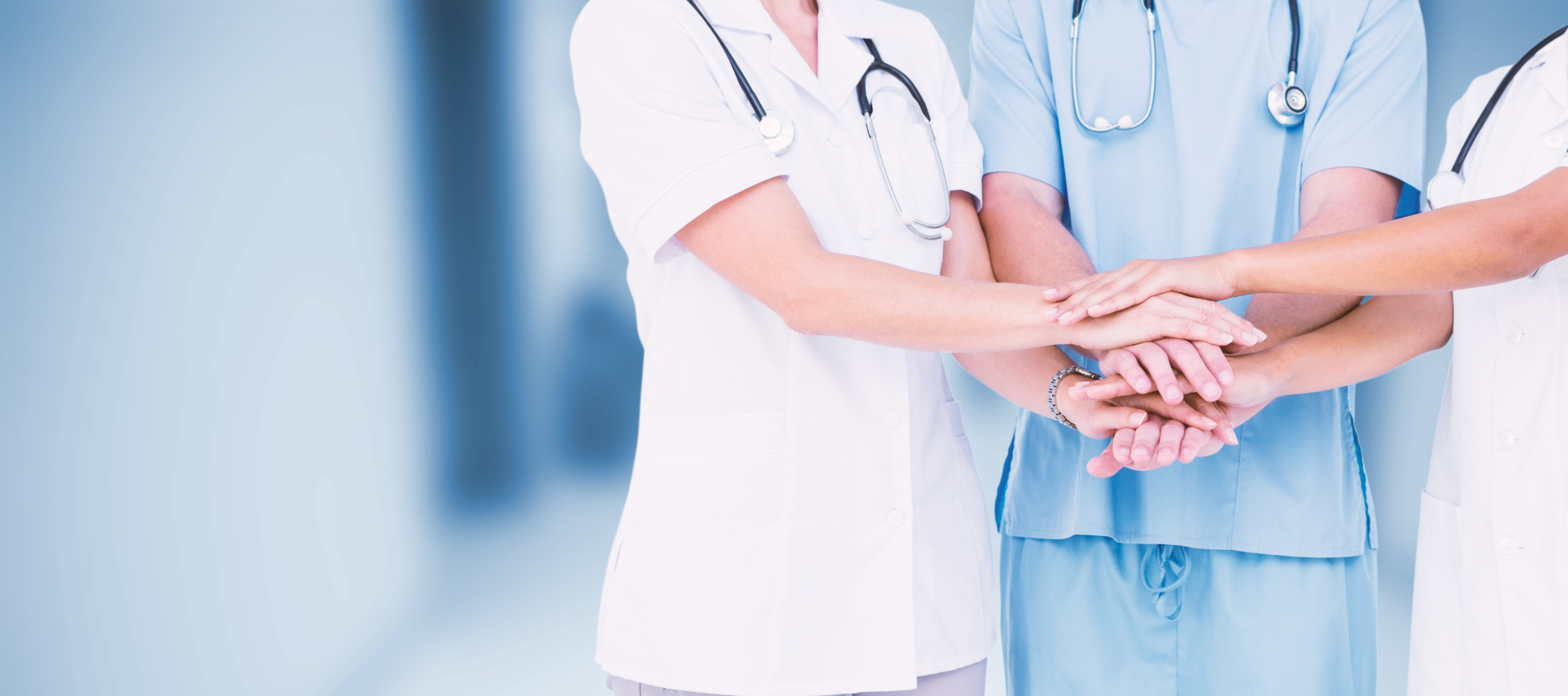 Healthcare professionals in scrubs and coats stacking hands in teamwork gesture.