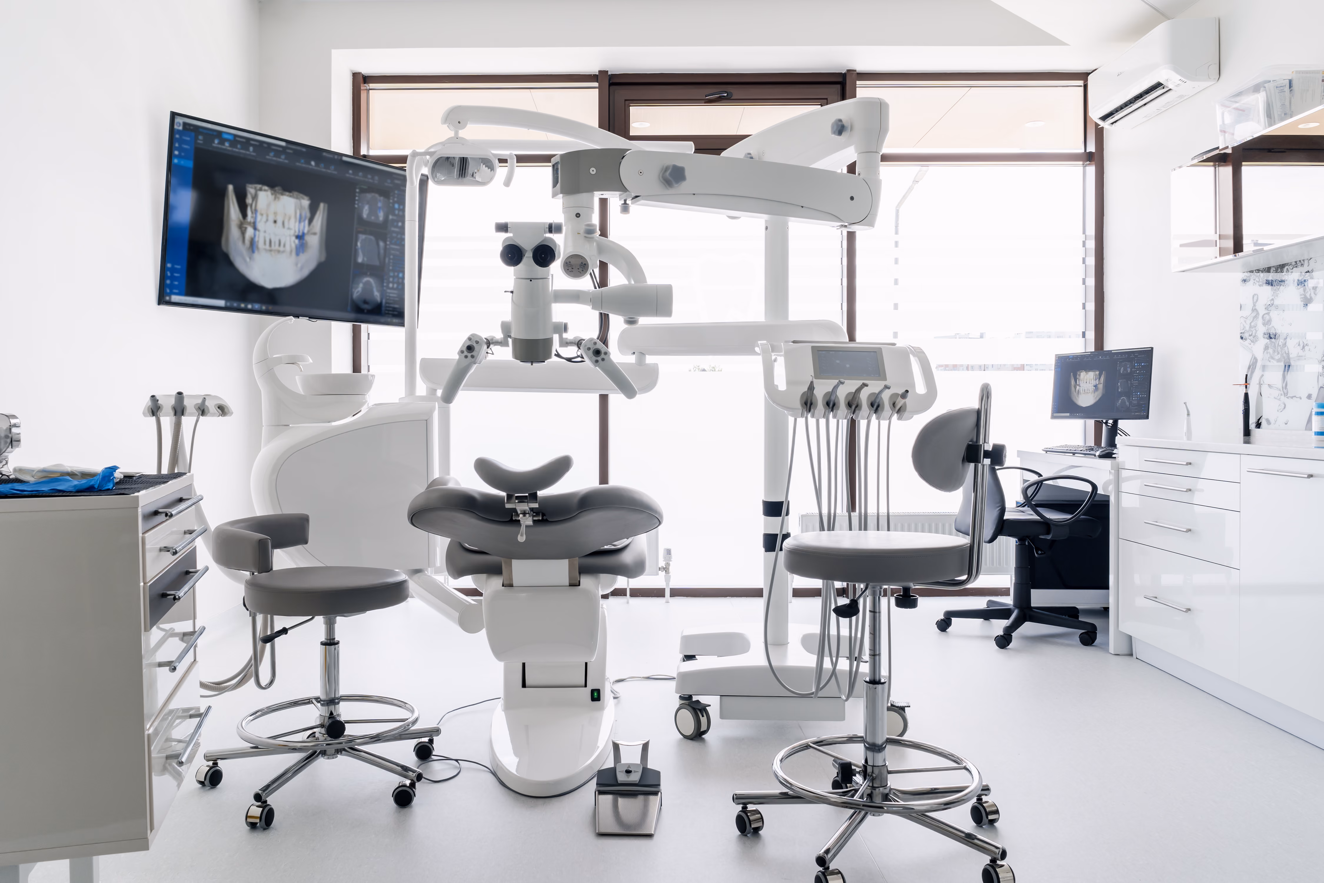 Modern dental clinic with chairs, instruments, and computer screens showing dental x-rays.