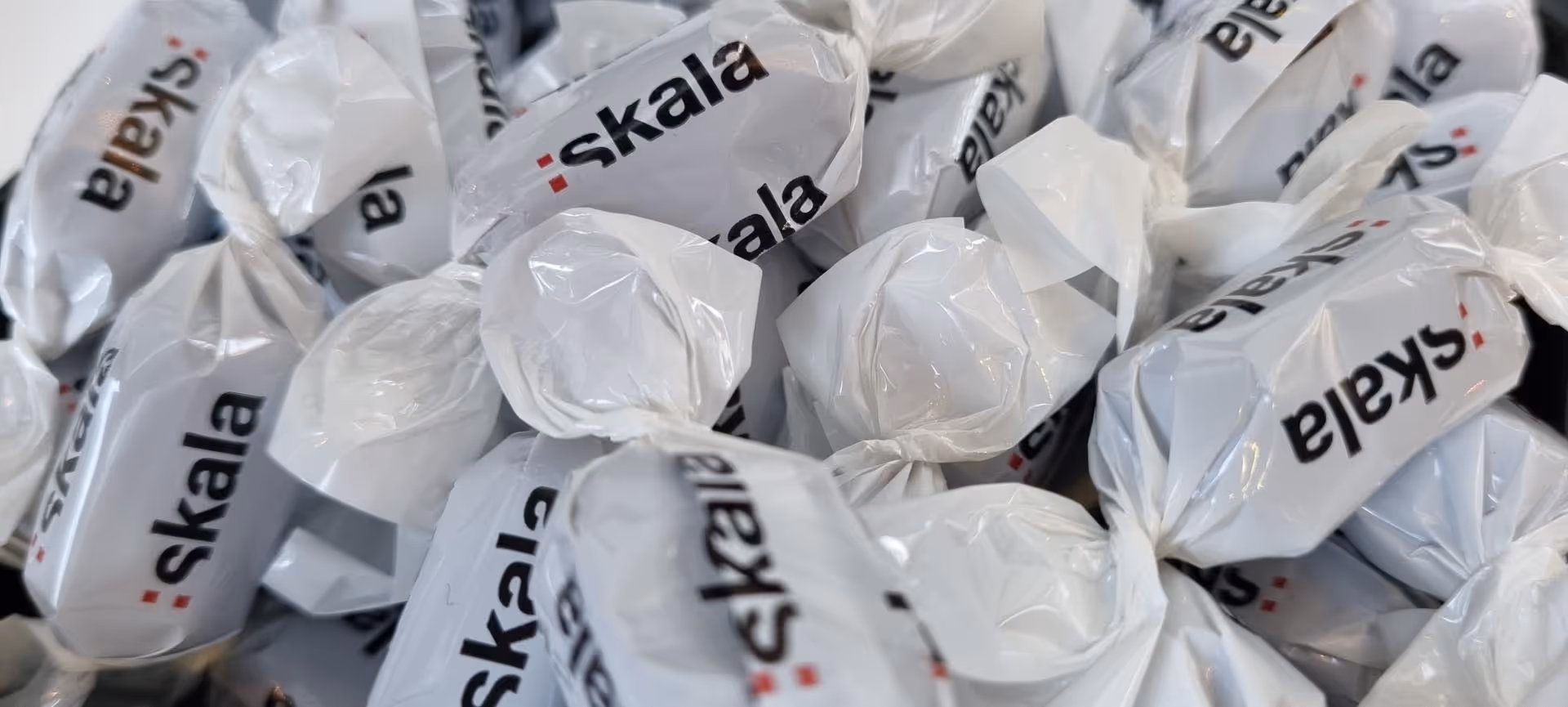 Flere hvite karameller pakket inn med merket Skala trykt på dem.