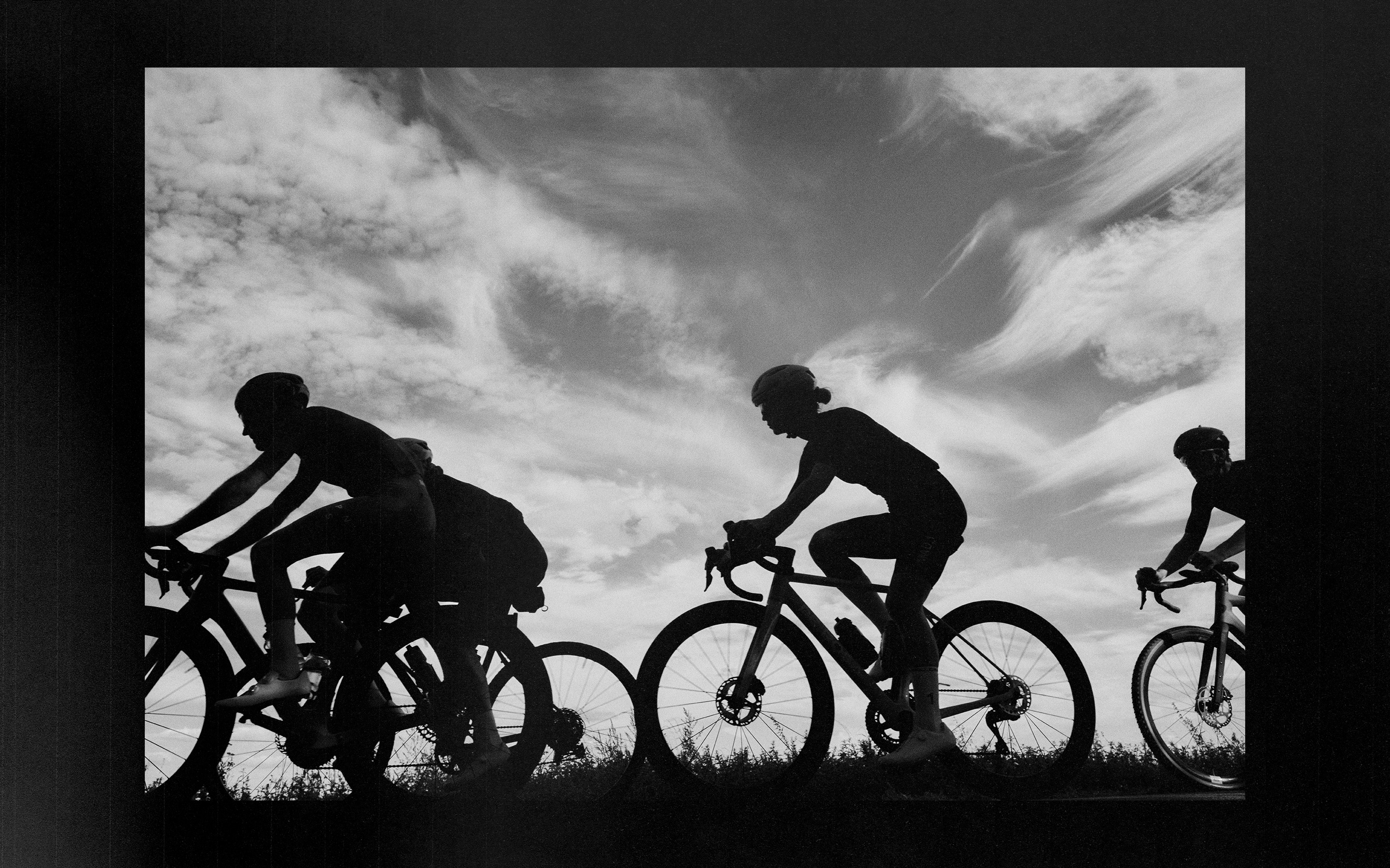 Black-and-white silhouettes of friends cycling beneath an open sky.