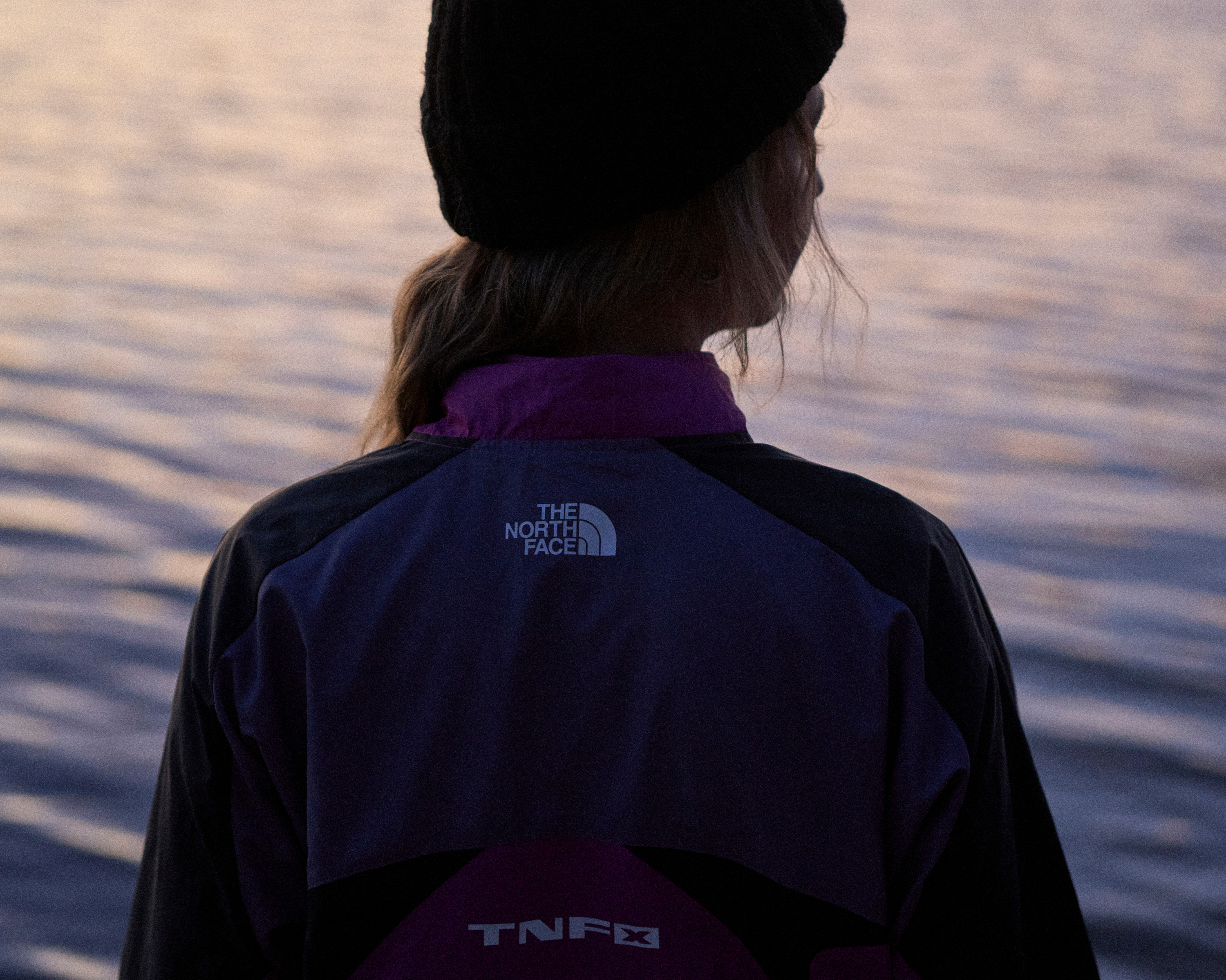 The North Face logo on the back of a purple outdoor jacket by the coast.