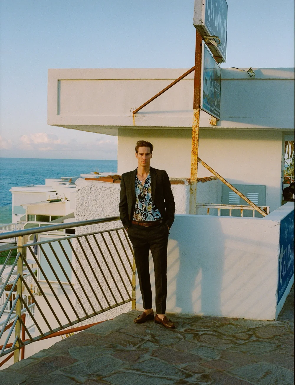 Full-length portrait of Patrick Pilz in a dark suit on a terrace overlooking the Mediterranean.