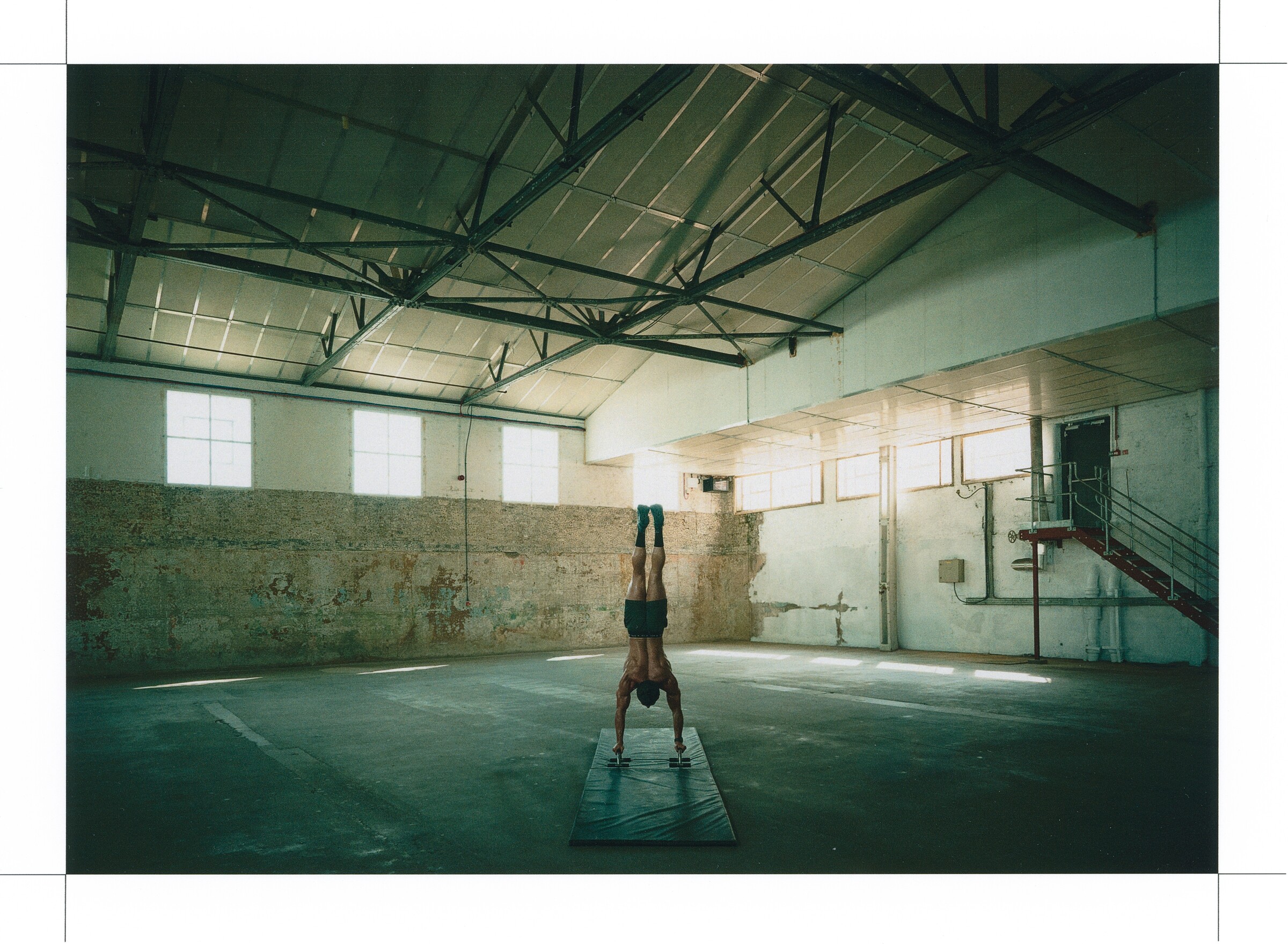 DESCENTE Athletic Originals: Athlete holding a handstand in a sunlit industrial training hall.