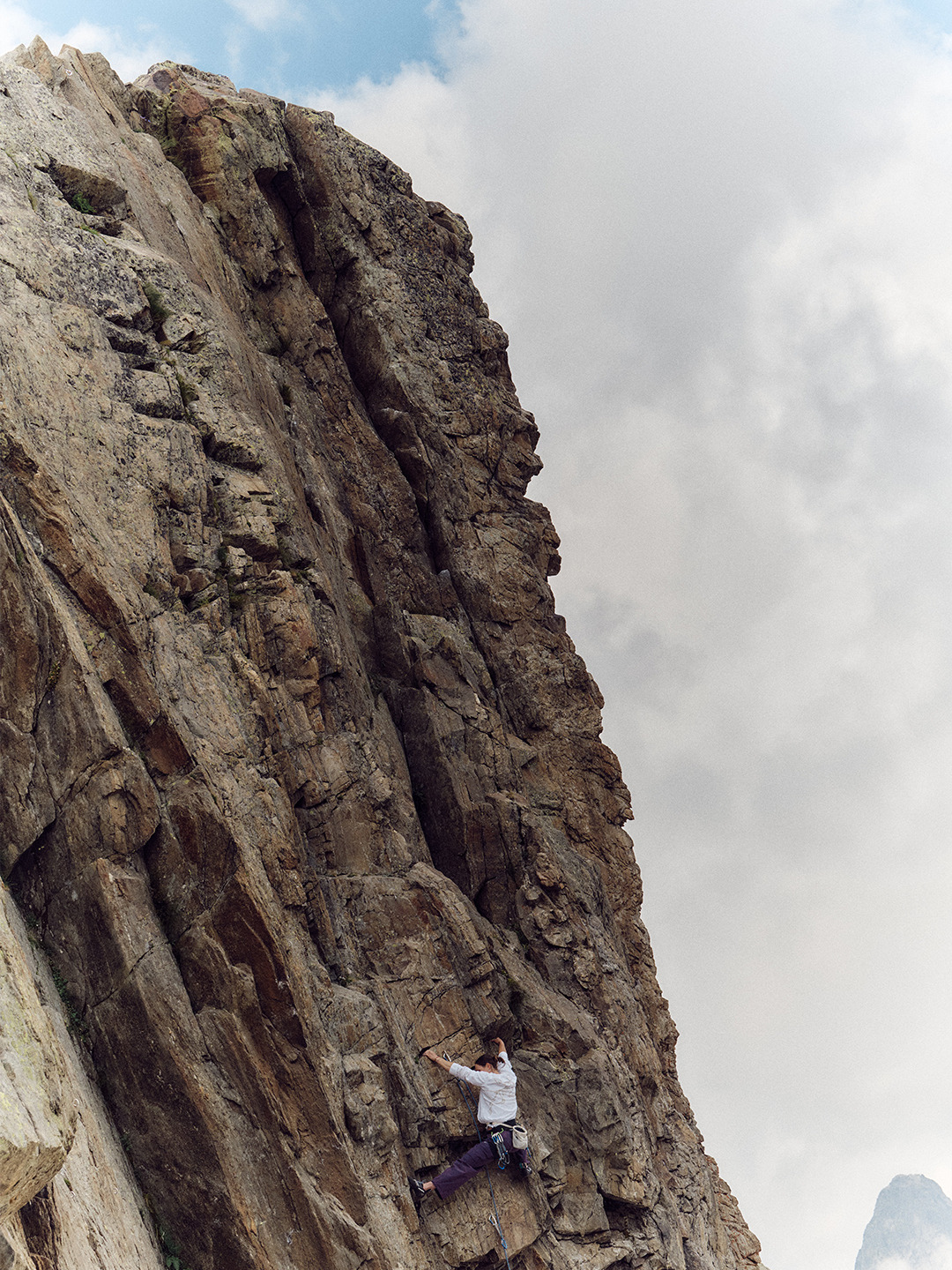 Arc'teryx Translating Flow State: Climber on a steep rock face beneath clouds.