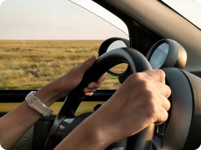 Hands on a steering wheel driving through open countryside