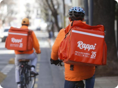 Rappi delivery riders with orange backpacks cycling through a city