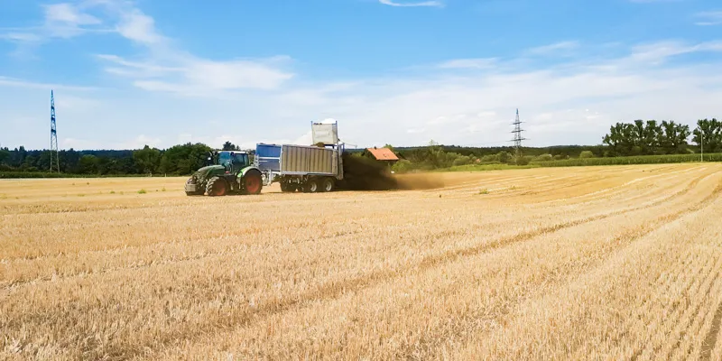 Traktor mit Anhänger bringt Kompost auf ein abgeerntetes Feld
