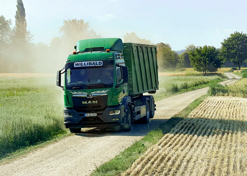 Grüner Willibald-Lkw mit Abrollcontainer auf einem Feldweg