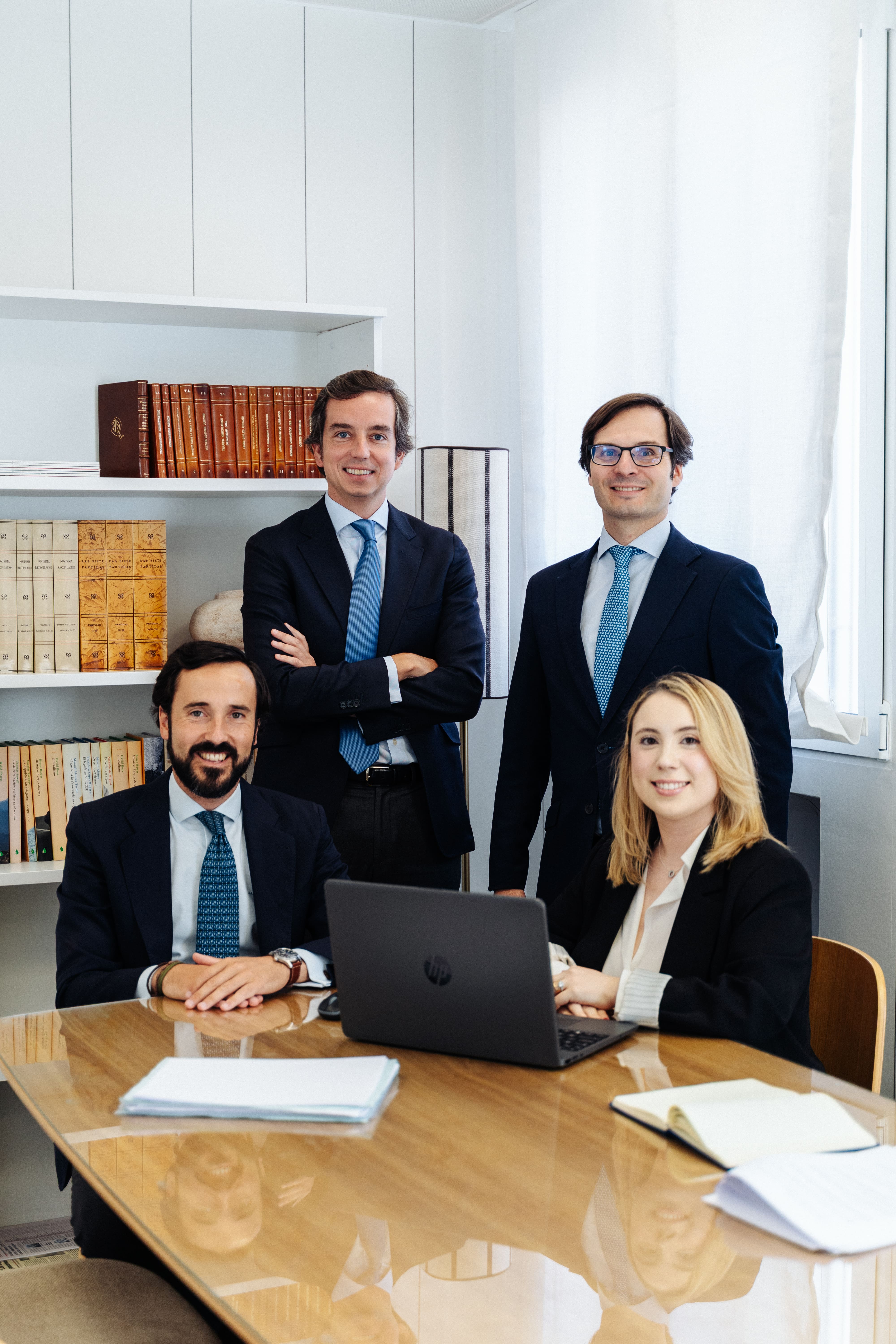 Cuatro profesionales de negocios vestidos formalmente en una oficina con computadora y libros.