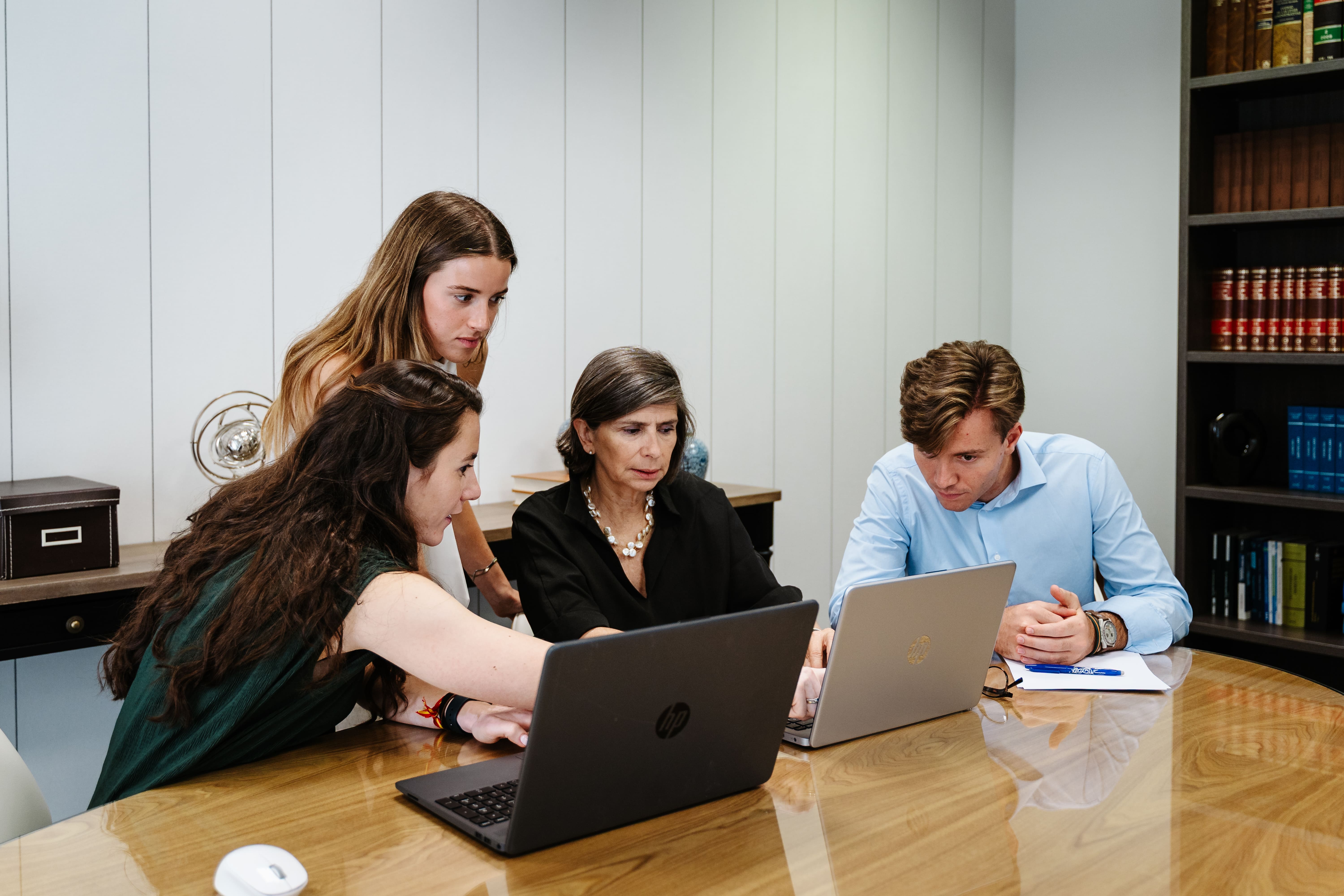 Cuatro personas en una reunión mirando y trabajando en laptops en una mesa de cristal redonda.