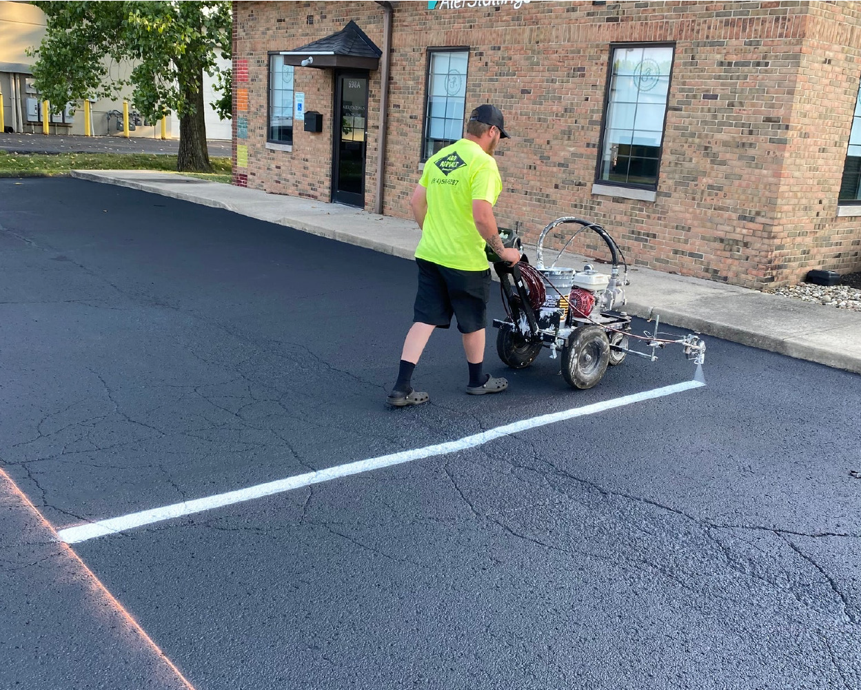 A&D Asphalt crew member using a line striping machine on a freshly sealcoated lot