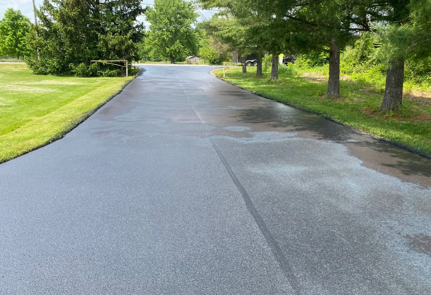 Freshly sealcoated residential asphalt driveway curing between green lawns
