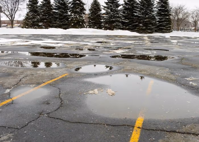 Standing water pooling on asphalt from poor parking lot drainage