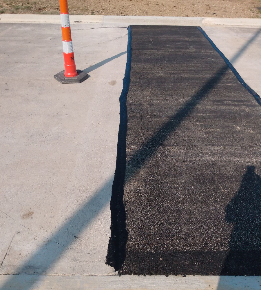 New asphalt patch repair beside a concrete curb with a traffic cone