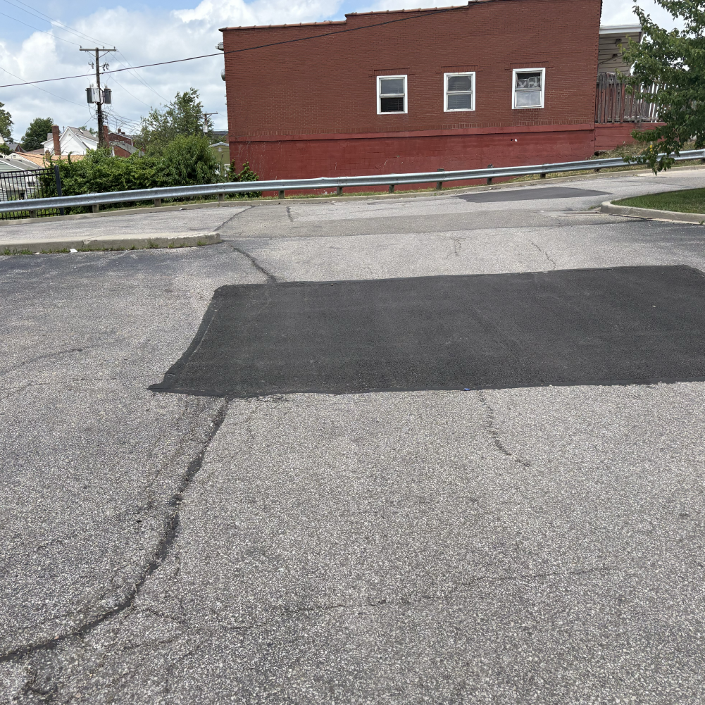 Large asphalt patch repair in a commercial parking lot next to a brick building