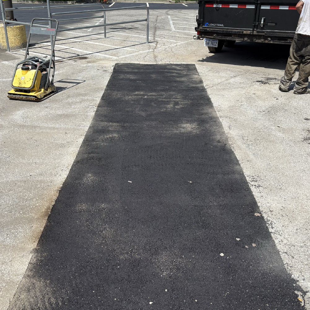 Fresh asphalt patch repair running through a damaged paved surface