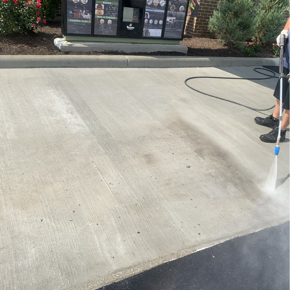 A&D Asphalt crew member pressure washing a concrete pad outside a commercial building