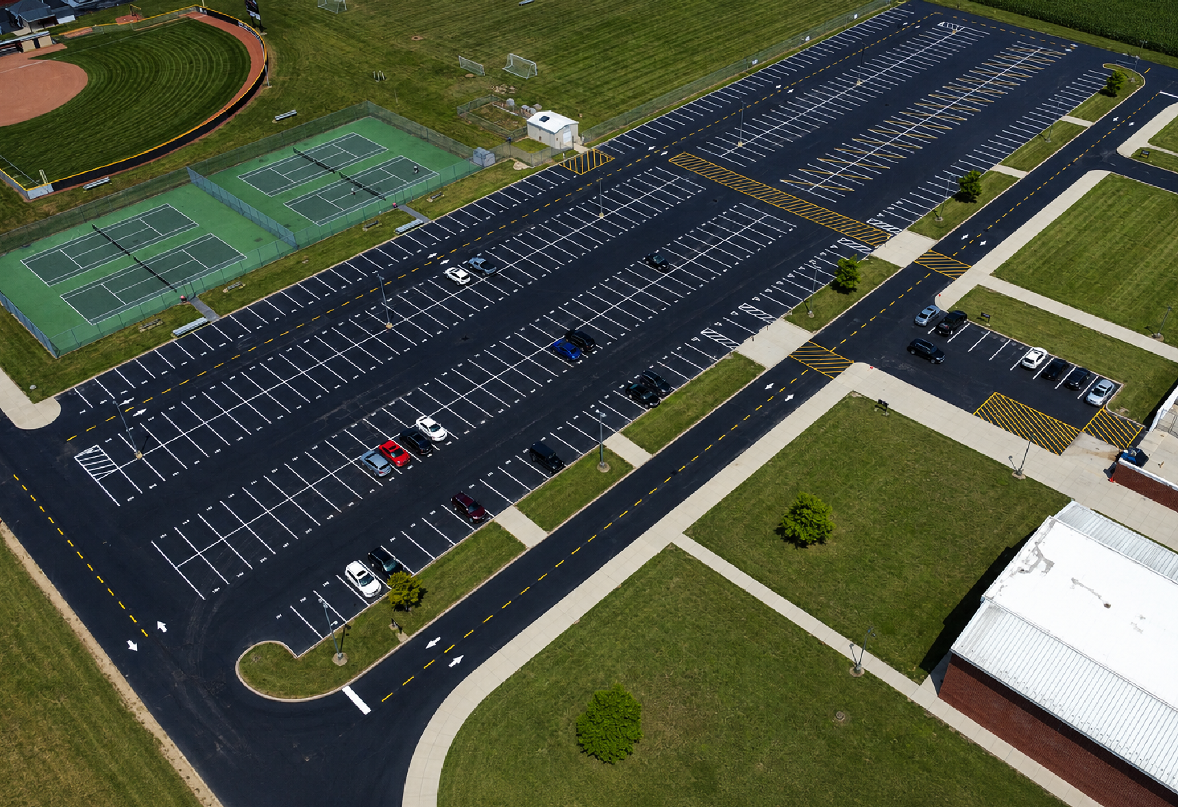 Aerial view of a large, freshly sealcoated and striped parking lot beside baseball fields and tennis courts