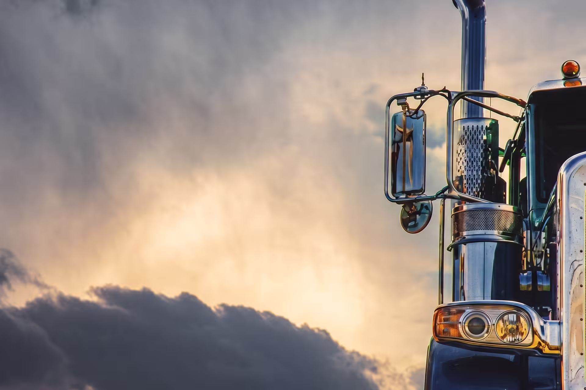 Close-up of a semi-truck's mirror and grille against a dramatic sunset sky