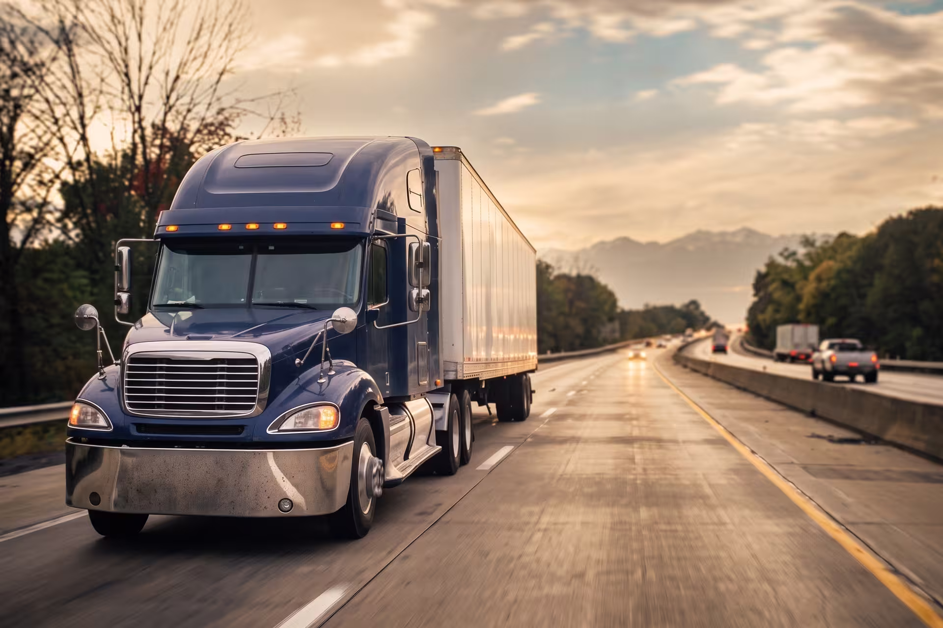 Semi-truck with trailer driving on a highway beneath a cloudy sky