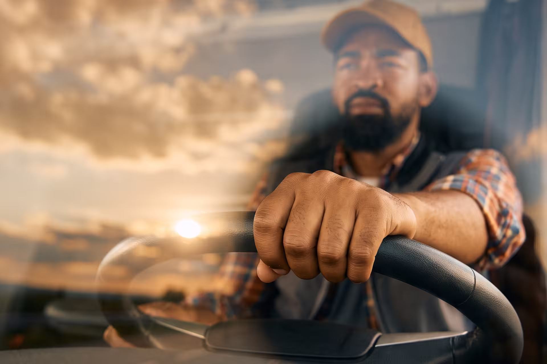 Close-up of a truck driver's hand gripping the steering wheel at sunset