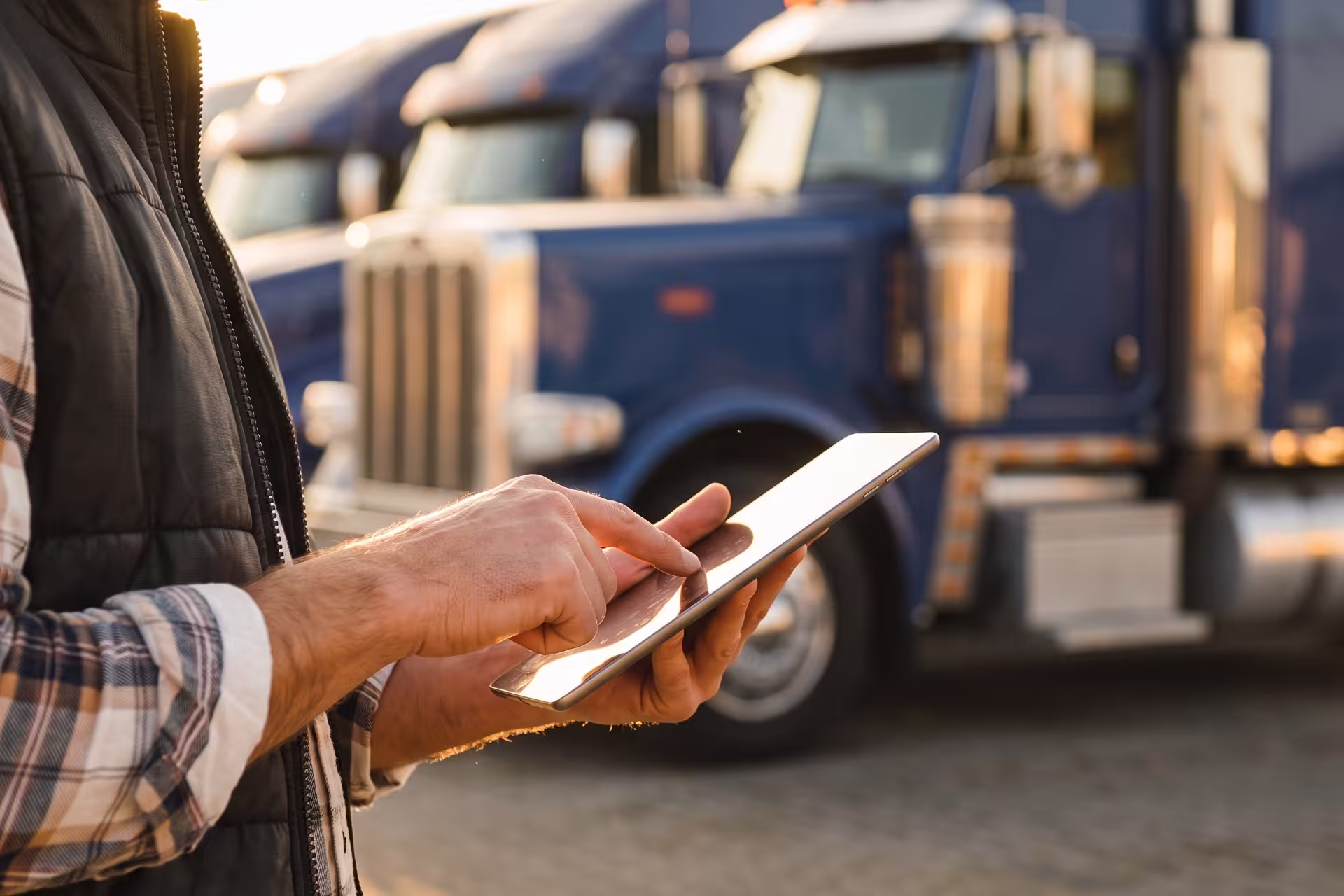 Close-up of a hand using a tablet in front of a parked semi-truck fleet