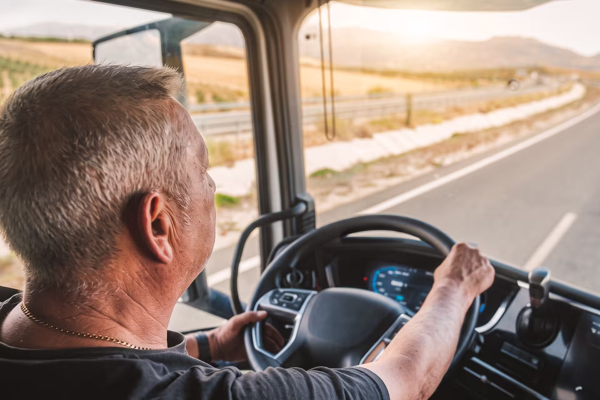 Over-the-shoulder view of a truck driver's hands on the wheel while driving