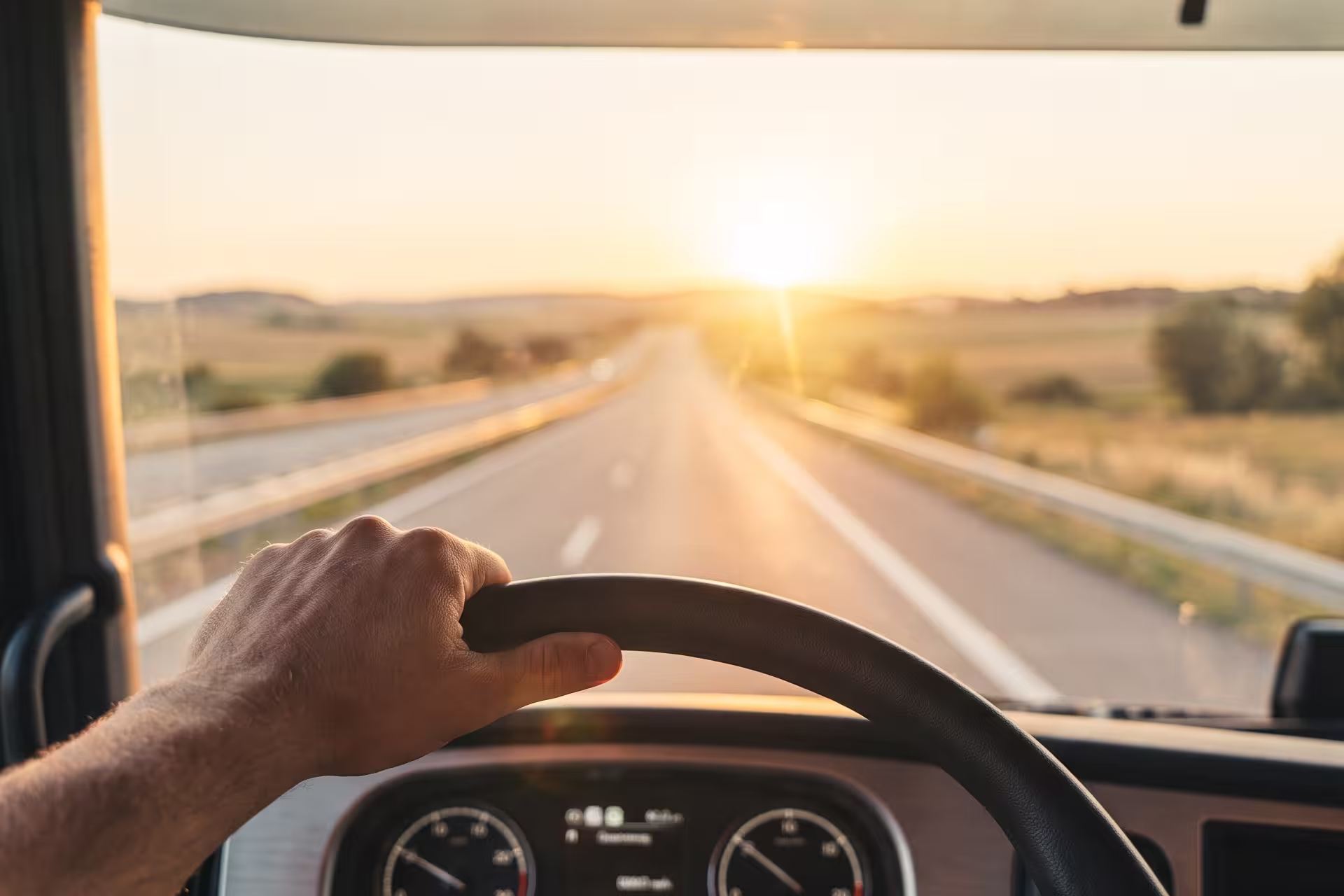 Driver's-eye view through a truck windshield of an open highway at sunrise