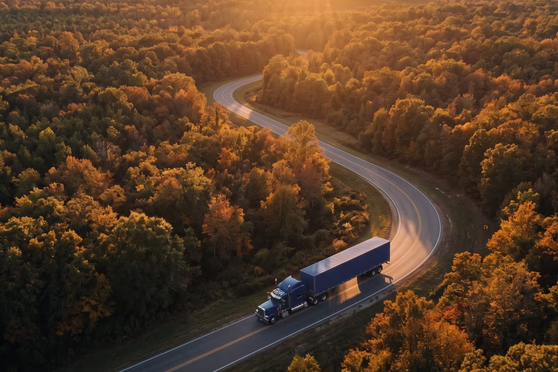 Aerial view of a semi-truck driving a winding road through autumn forest