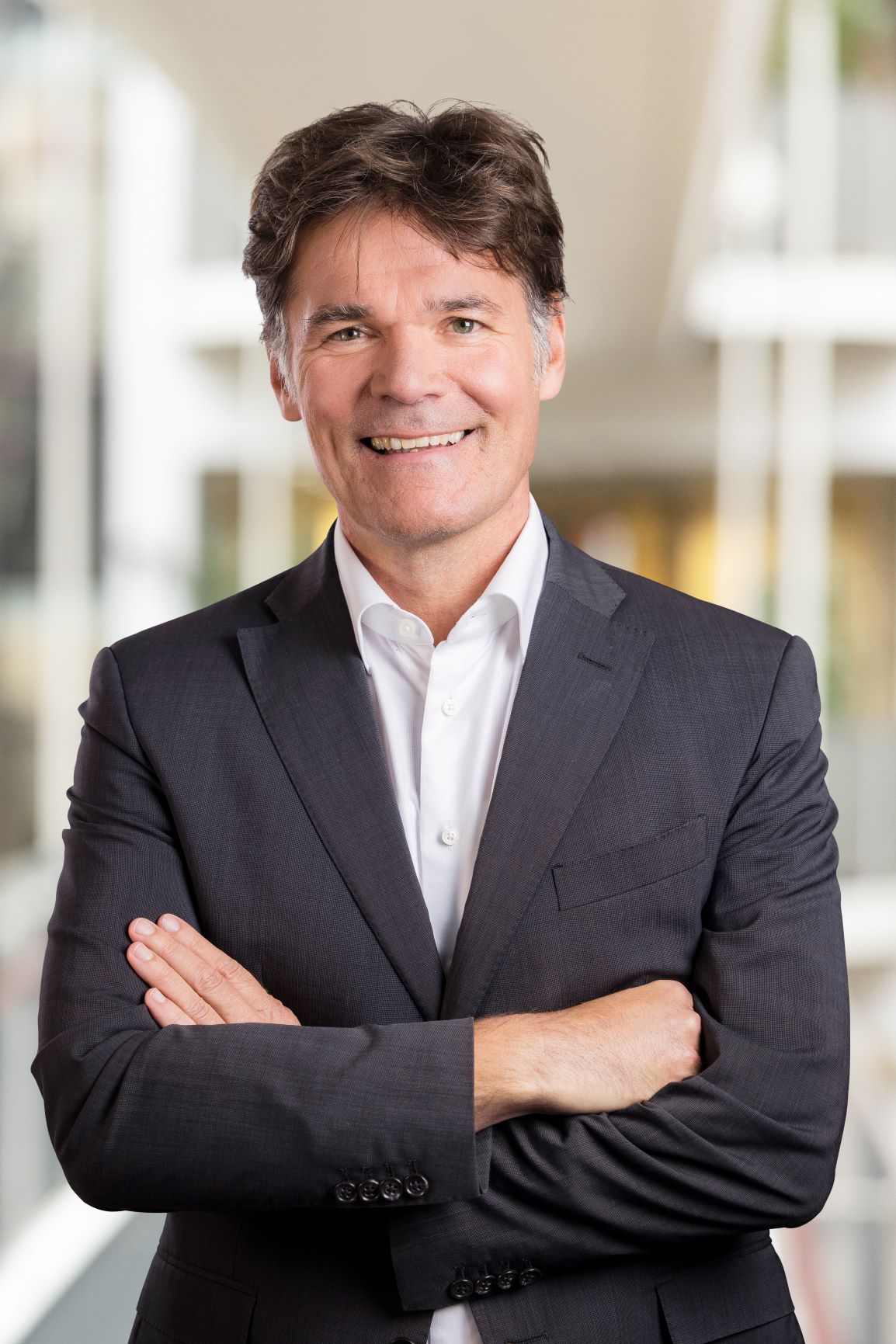 Portretfoto van Susan met krullend bruin haar, in een gemêleerde blazer over een paarse top, glimlachend met een hand in haar zij.