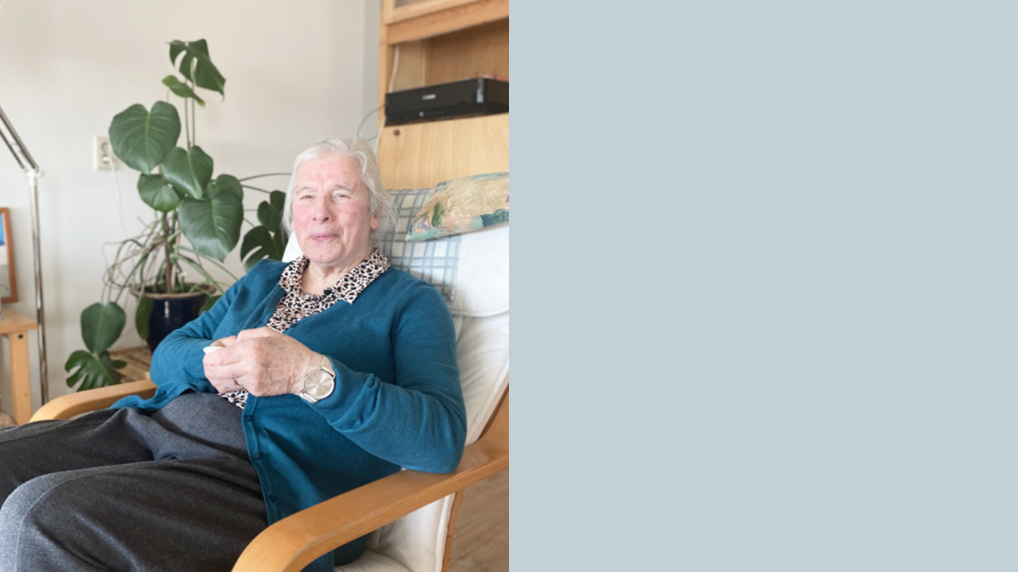 Portretfoto van een vrouw met een bril en groene blazer, voor een achtergrond van groen struikgewas.