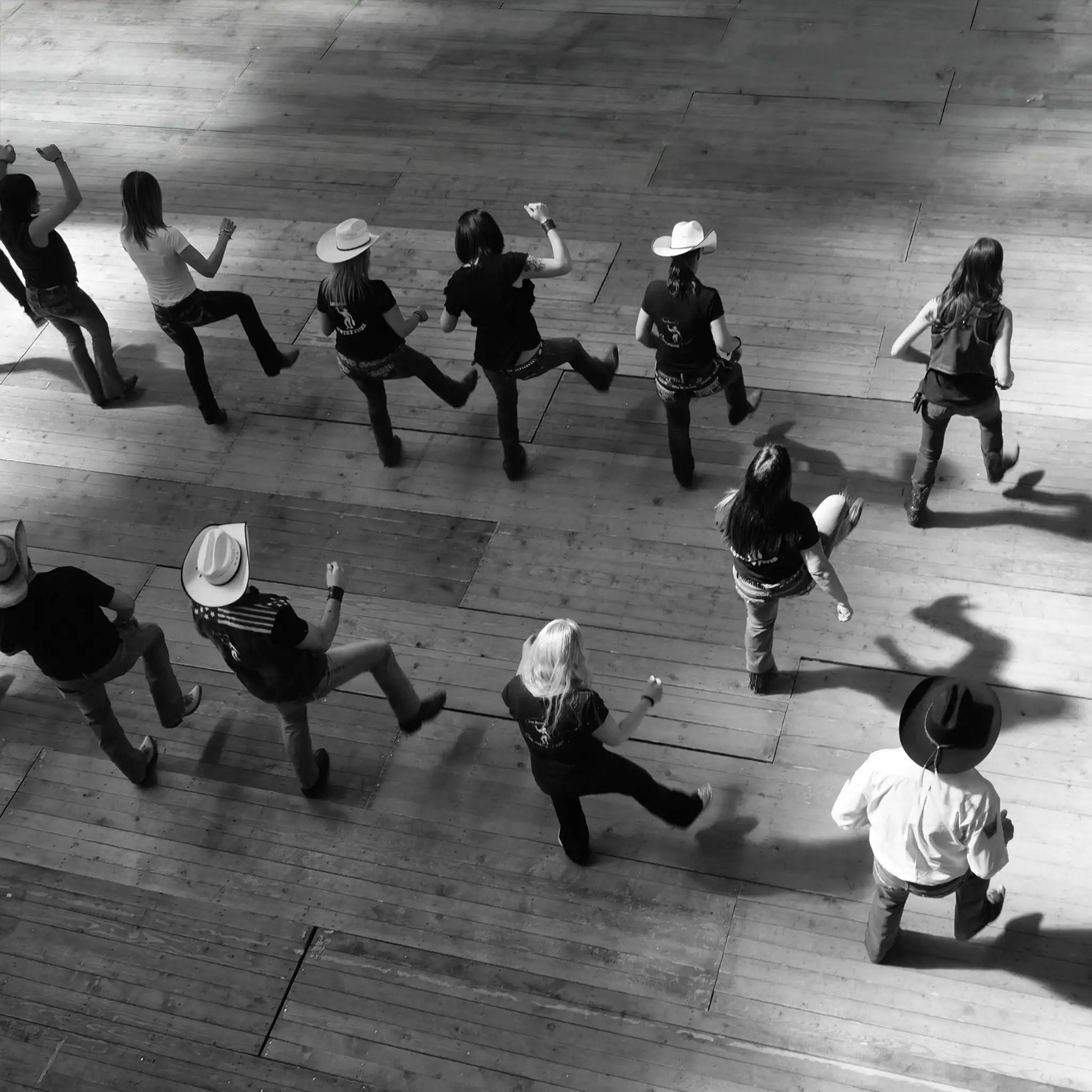 Vue de haut d'un groupe qui danse en ligne, plusieurs coiffés d'un chapeau de cowboy, pendant un cours de danse country à l'École de Danse M3 de Cowansville.