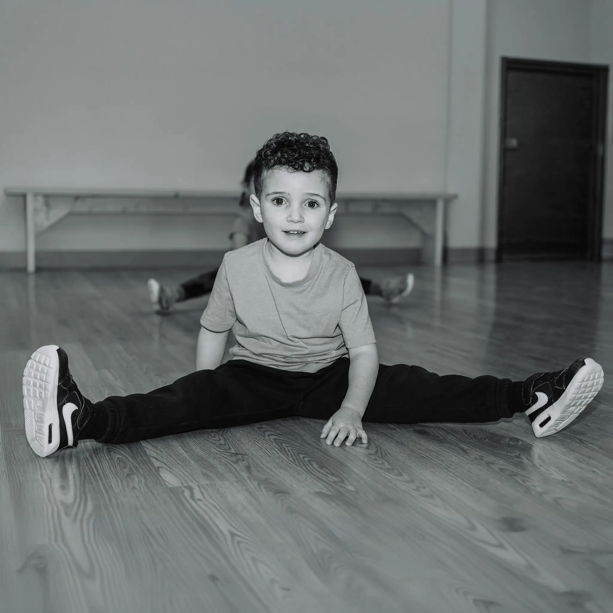 Jeune garçon assis au sol, jambes écartées en grand écart, souriant pendant un cours d'initiation à la danse à l'École de Danse M3 de Cowansville.