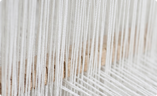 Close-up of white threads vertically woven on a loom with wooden parts visible in the background.