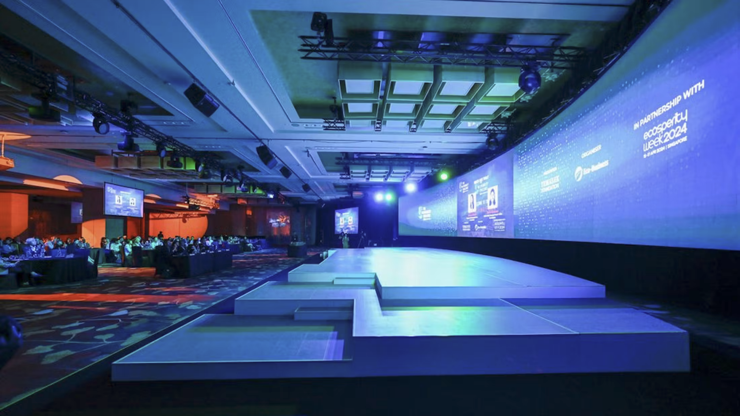 Large modern stage with tiered platforms and illuminated screens in a conference hall with seated audience.