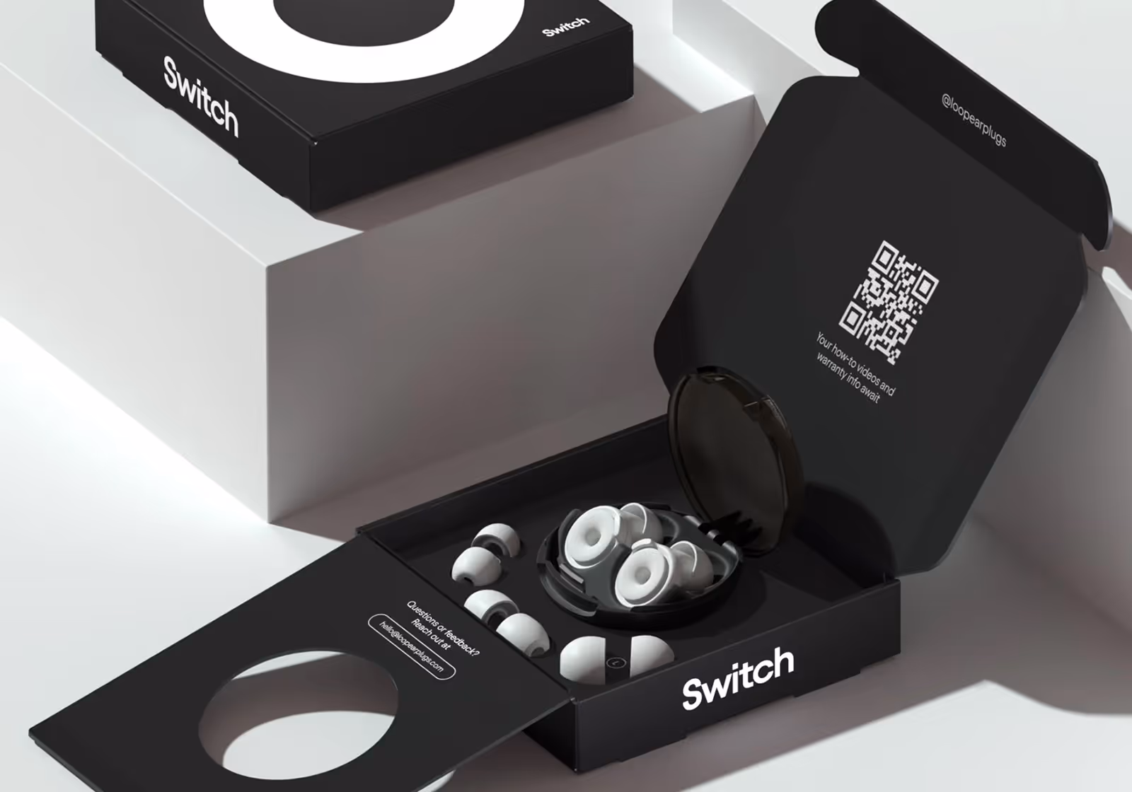 Switch earplugs packaging box open with multiple white earplugs and a round black case inside.