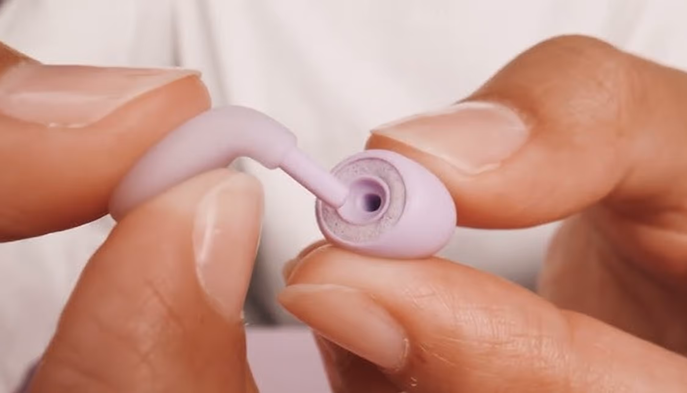 Close-up of hands inserting a small pink ear tip into a wireless earbud.