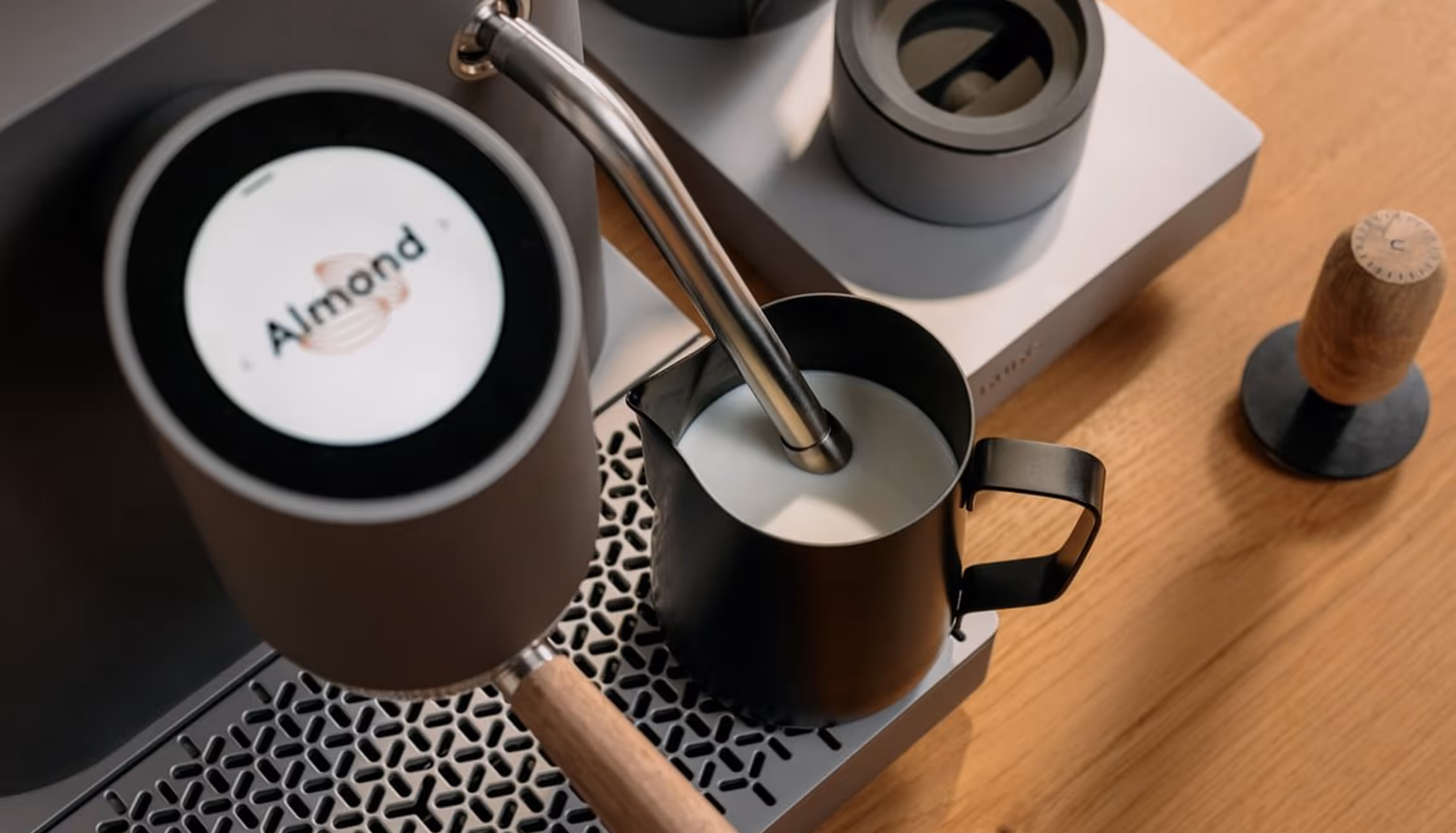 Coffee machine with almond milk steaming wand in a black pitcher on a wooden surface