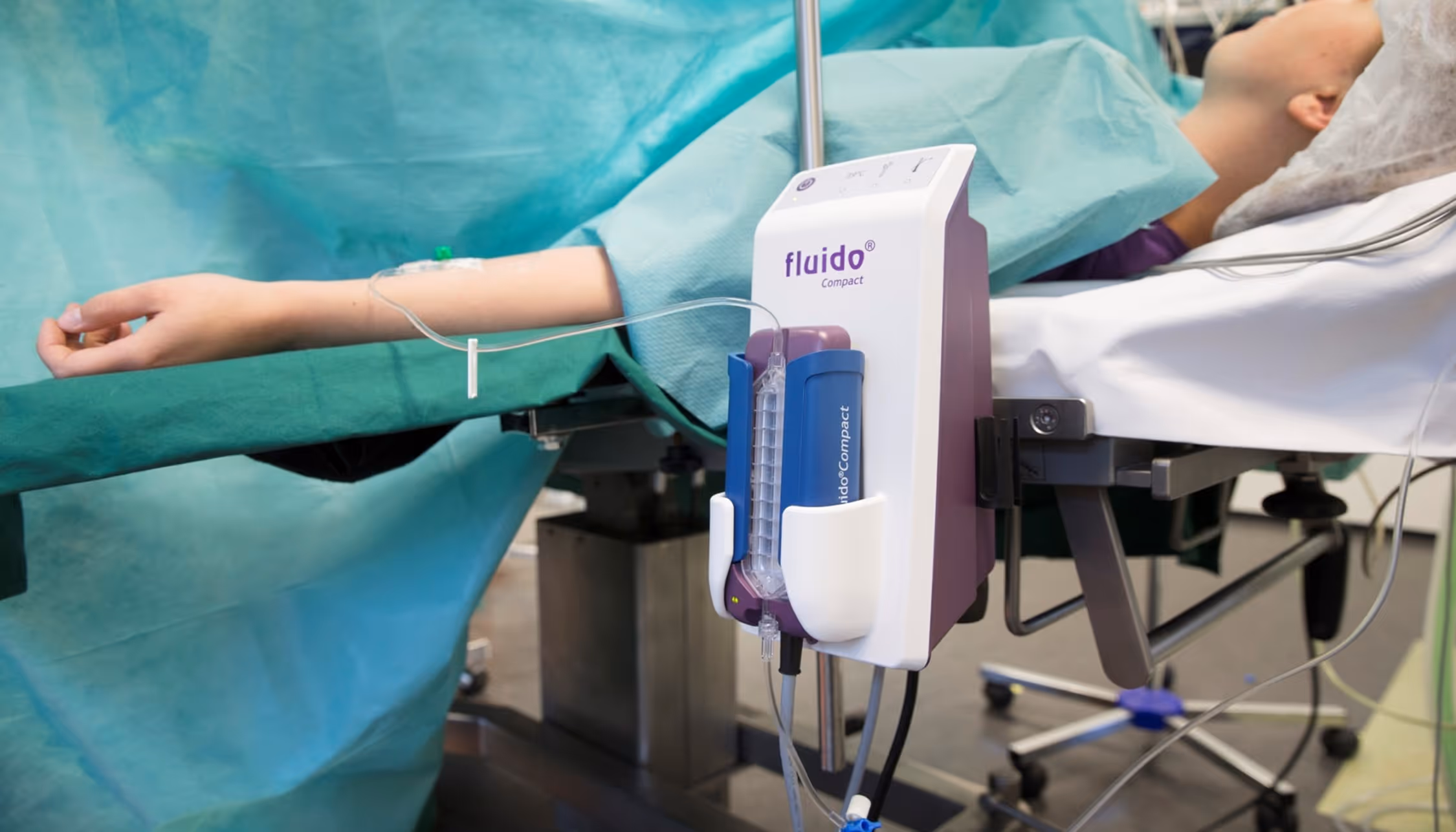 Patient lying on hospital bed with intravenous line connected to a Fluido Compact medical device.