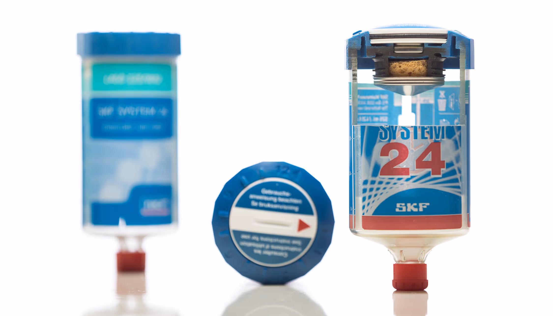 Three blue lubricant dispensers labeled SYSTEM 24 SKF with red caps on a reflective white surface.