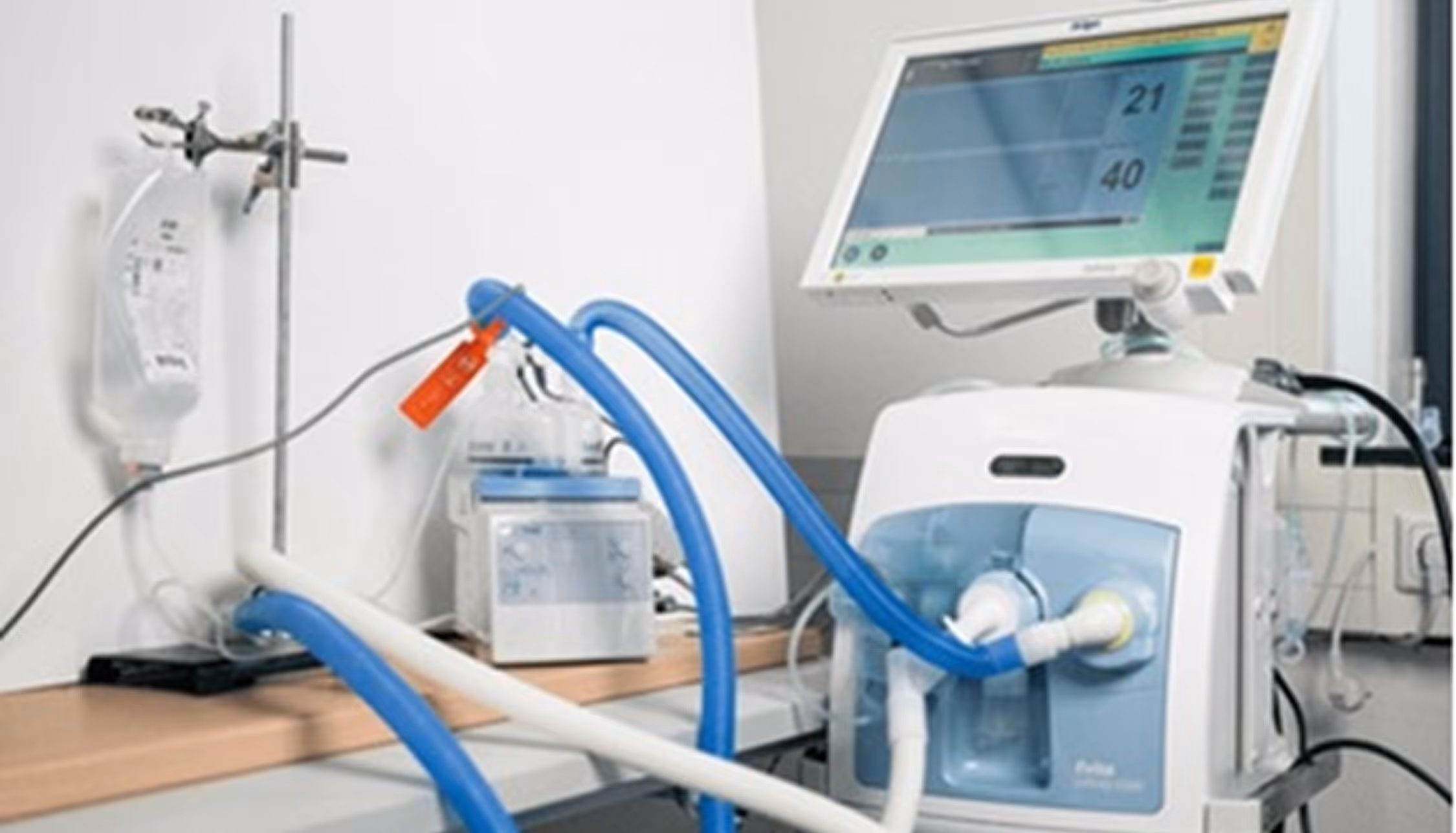 Medical ventilator machine with tubes and a monitor showing breathing parameters in a clinical room.