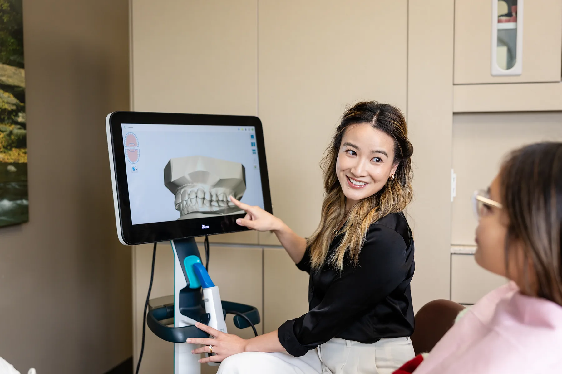 A dental team member pointing out a 3D scan of a patient's teeth on a chairside monitor