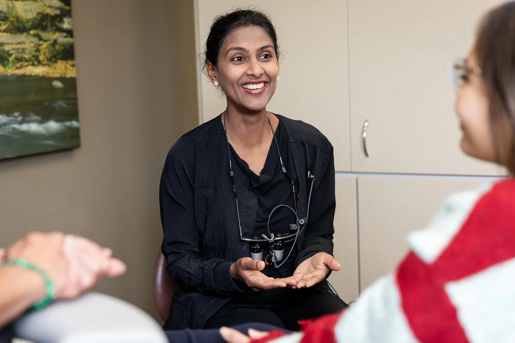 A dentist sitting and talking with a patient, hands open mid-explanation