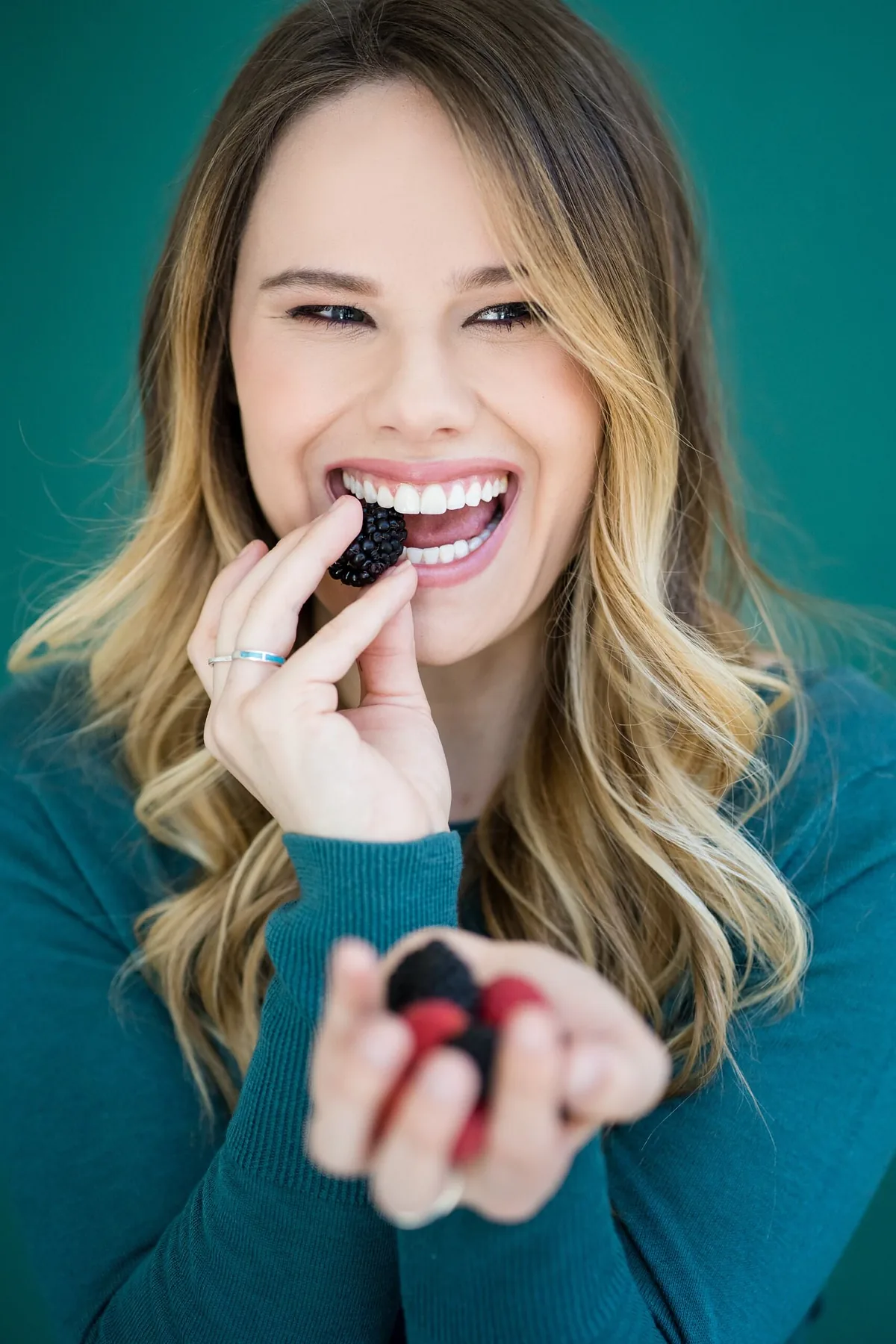 A woman biting into a blackberry, smiling