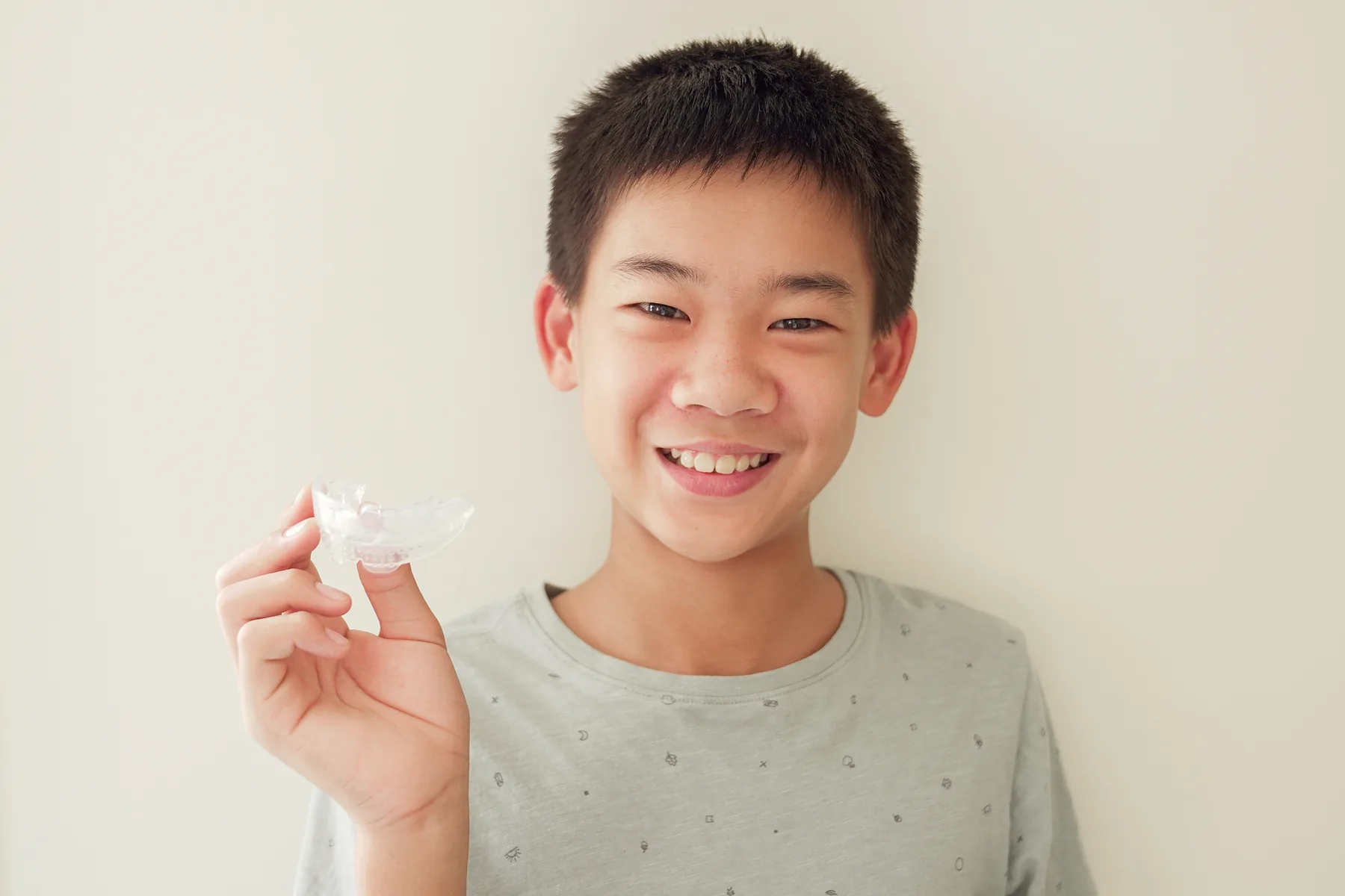 A boy holding up his clear retainer and smiling