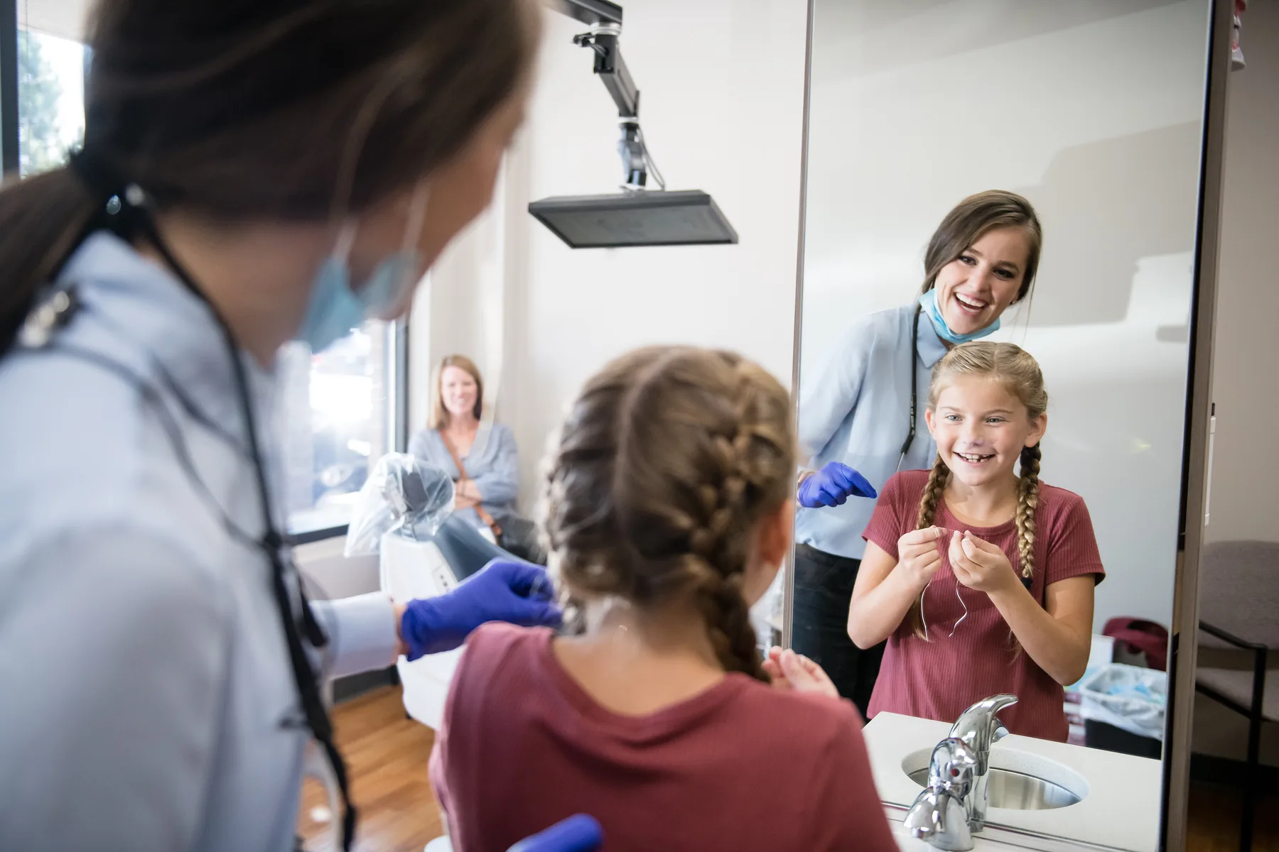 A girl at the sink with her hygienist while her mother watches from across the room