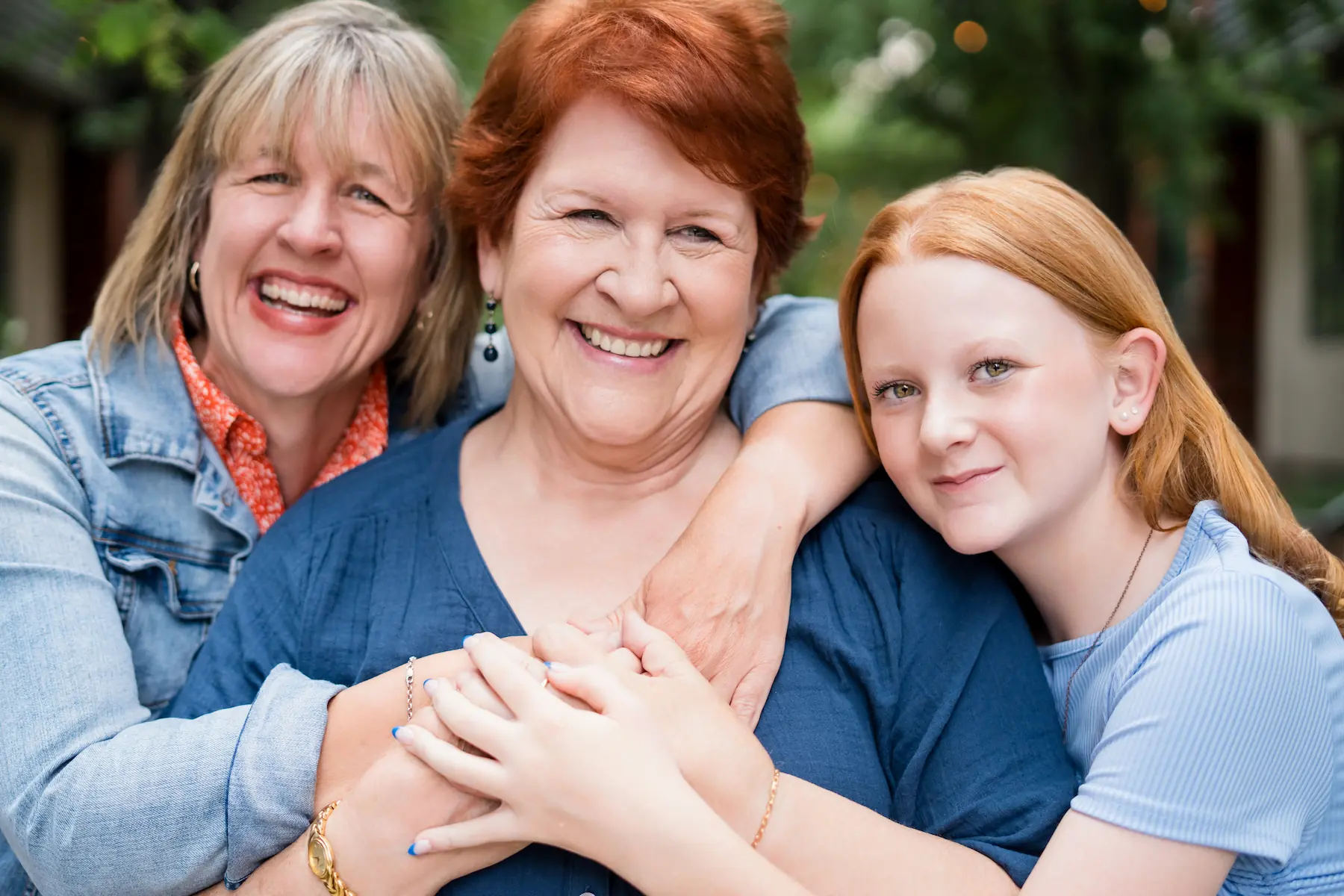 Three generations of women smiling and hugging outdoors, showing love and family bond.
