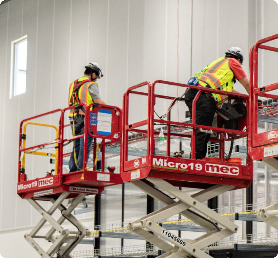 Electrical crews on scissor lifts installing overhead infrastructure in a data hall.