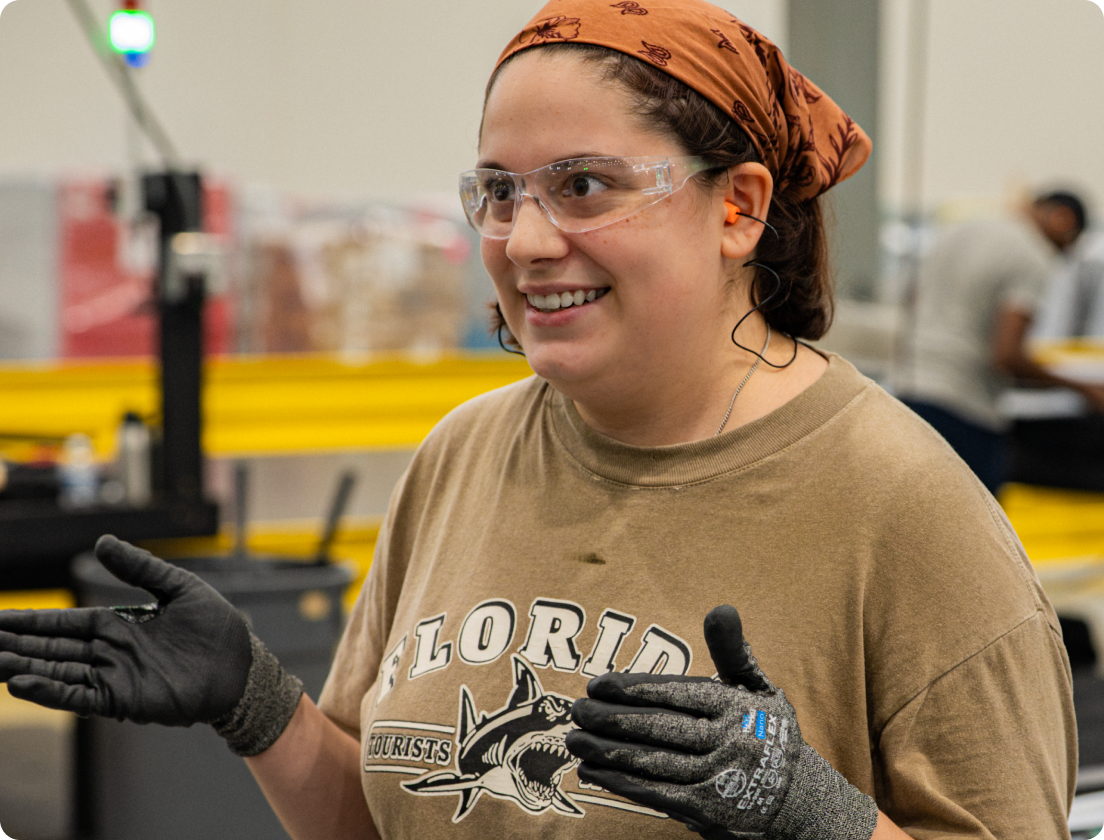 A trainee in safety glasses smiling on the manufacturing floor