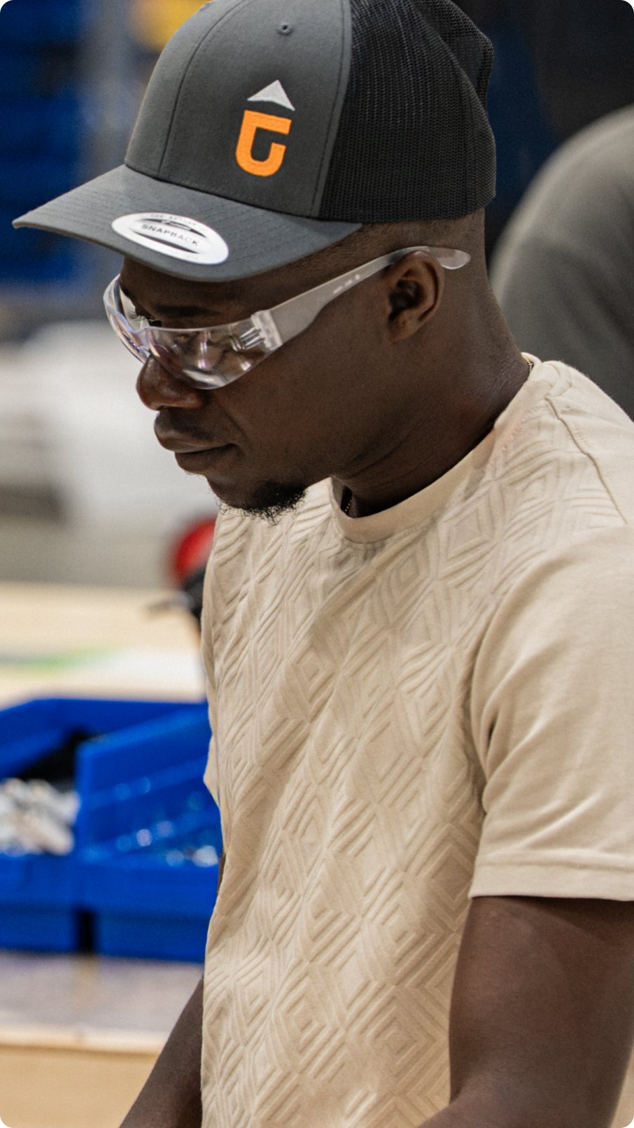 A team member in safety glasses and a branded cap working at a production bench
